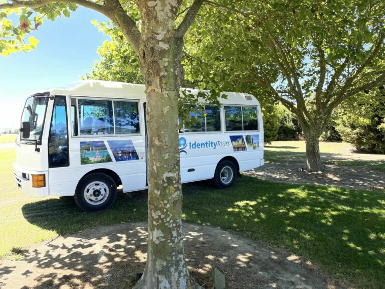 A photo of the Identity Tours bus parked. A tree is in the foreground