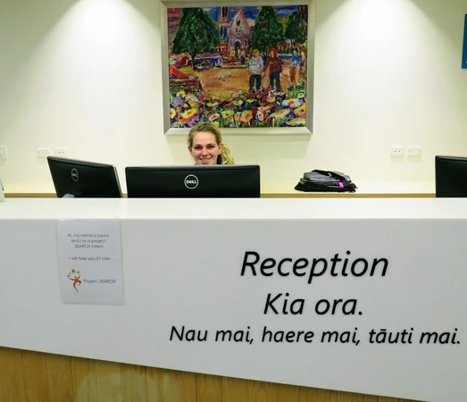 A woman sat at a desk. The desk has "Reception" written on it
