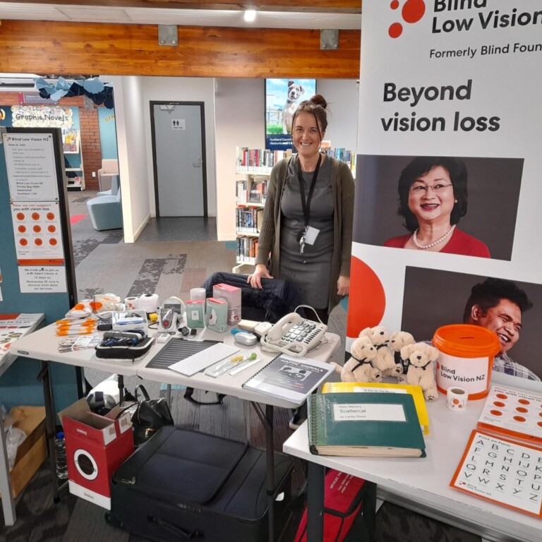 A woman standing at a stand with information to raise awareness on the blind low vision community