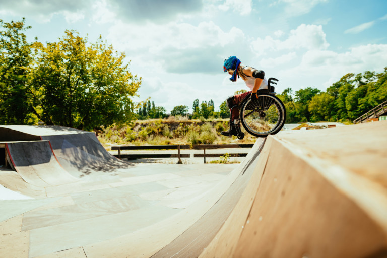 Woman in wheelchair rolls down hills in skatepark