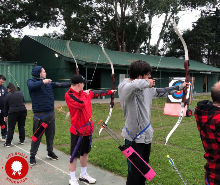 Three people with bows preparing to fire arrows at targets