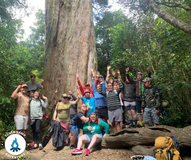Several people posed for a group photo in a forest. A large tree stands behind them