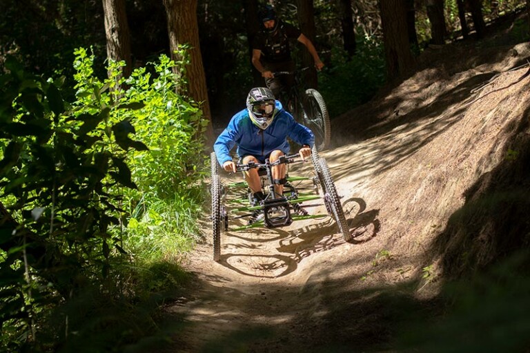 A photo of a person using the gravity quad bike. It is taken front on as they come down a dirt path. They are wearing a full-face helmet and a blue hoodie