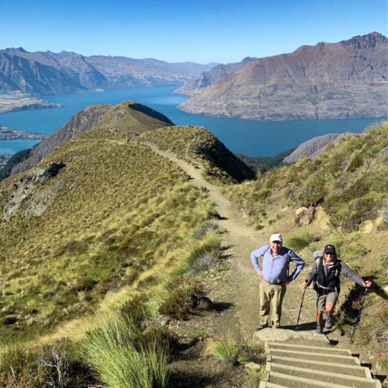 A photo of two people with hiking gear near the summit of a mountain walking trail. The weather is clear and sunny
