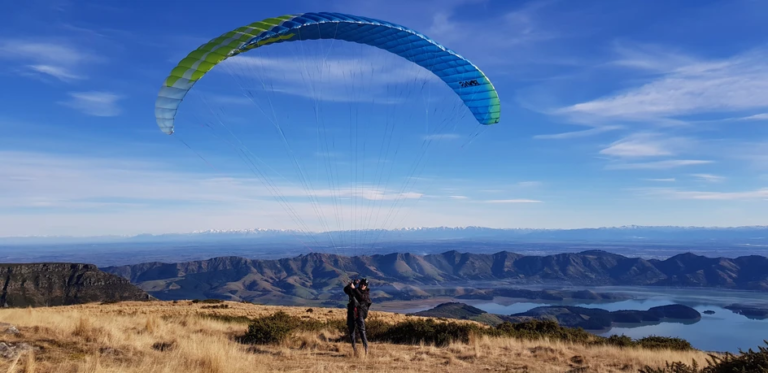 A wide shot of a person with a paraglider. The person remains on the ground with the paraglider aloft.