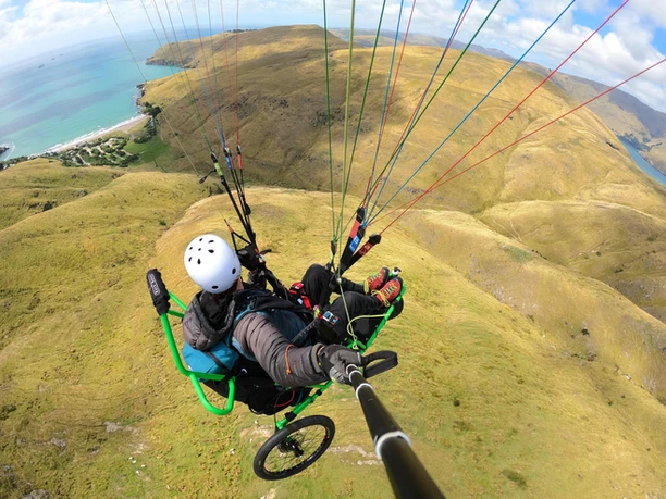 A photo of someone paragliding solo using an accessible tricycle wheelchair.